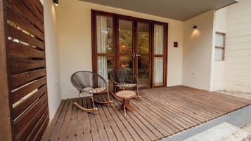 Terraza de madera con dos mecedoras y una mesita, que conduce a una puerta de cristal con cortinas.