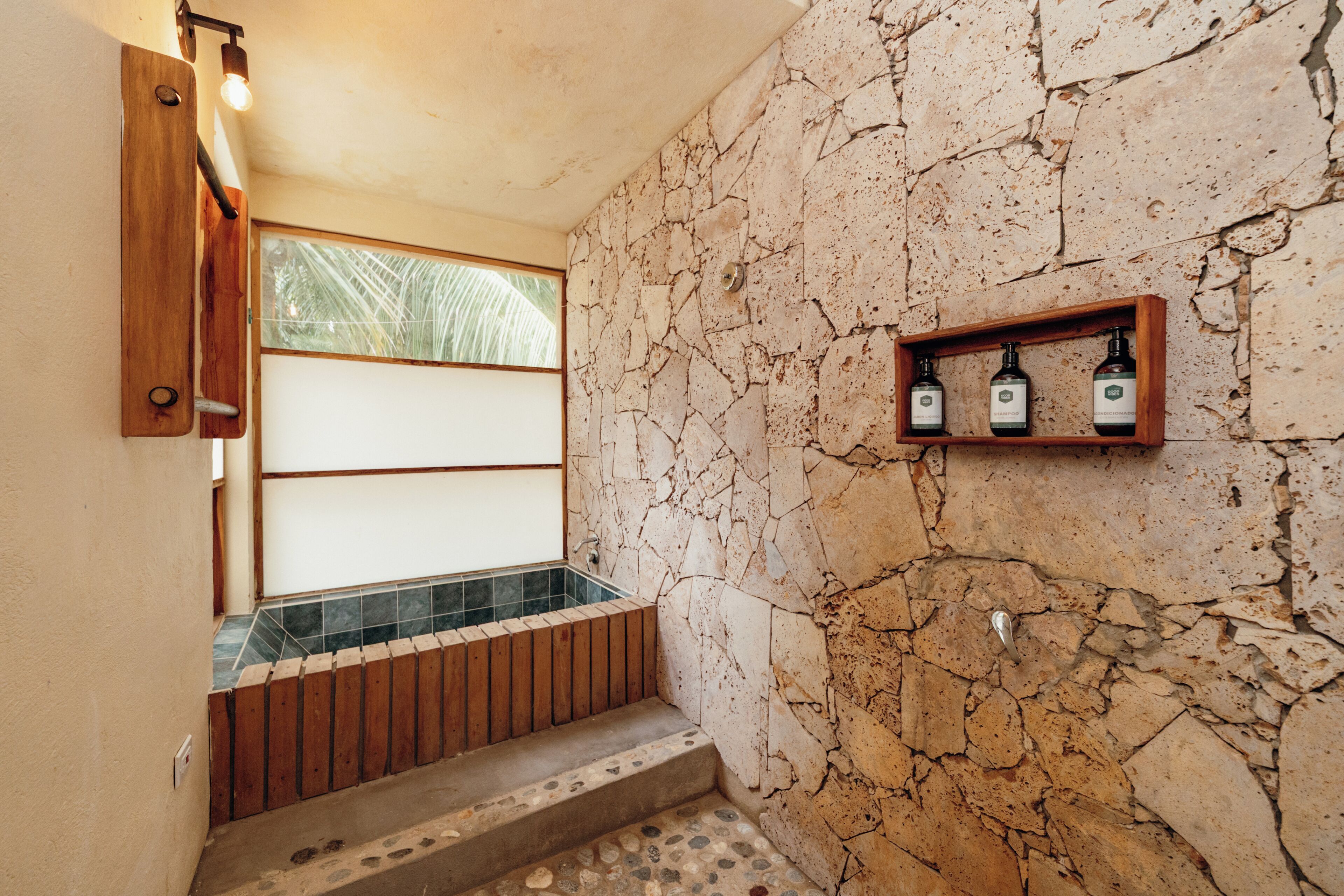 A bathroom with a stone wall, a wooden bench, and a shelf with toiletries.