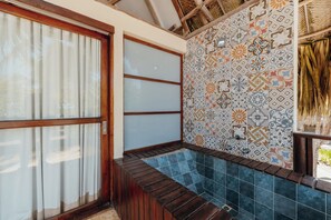 Un baño con banco de madera, bañera y pared revestida de azulejos con diseño geométrico.