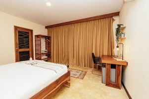 Een slaapkamer met een bed, een bureau, een stoel, een hangplant en een raam met gordijnen.
