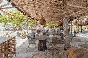 An outdoor seating area with tables and chairs, a thatched roof, and potted plants. - Tay beach hotel - Tayrona (Santa Marta)