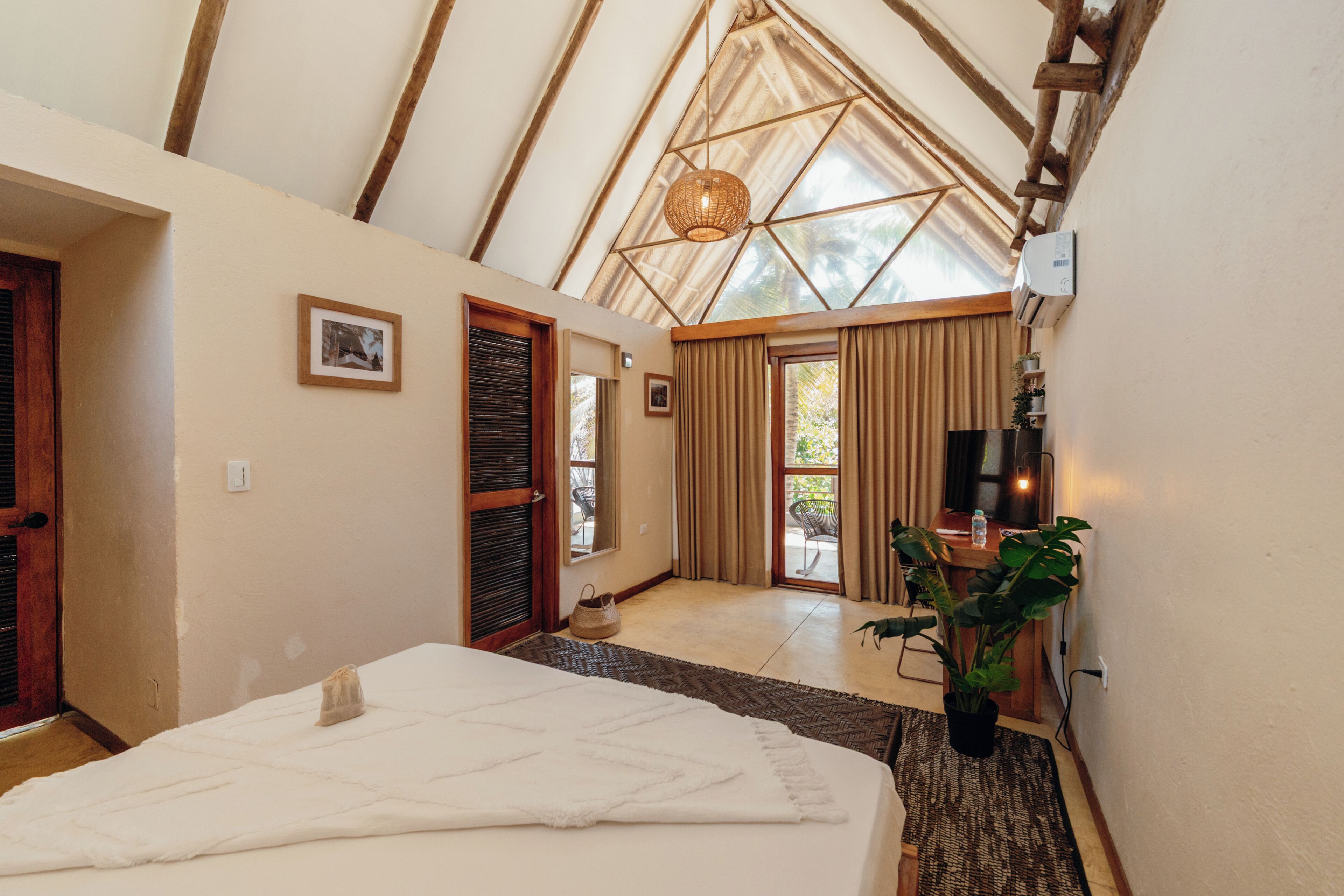 Un dormitorio con cama, lámpara colgante, puerta y vista al exterior.