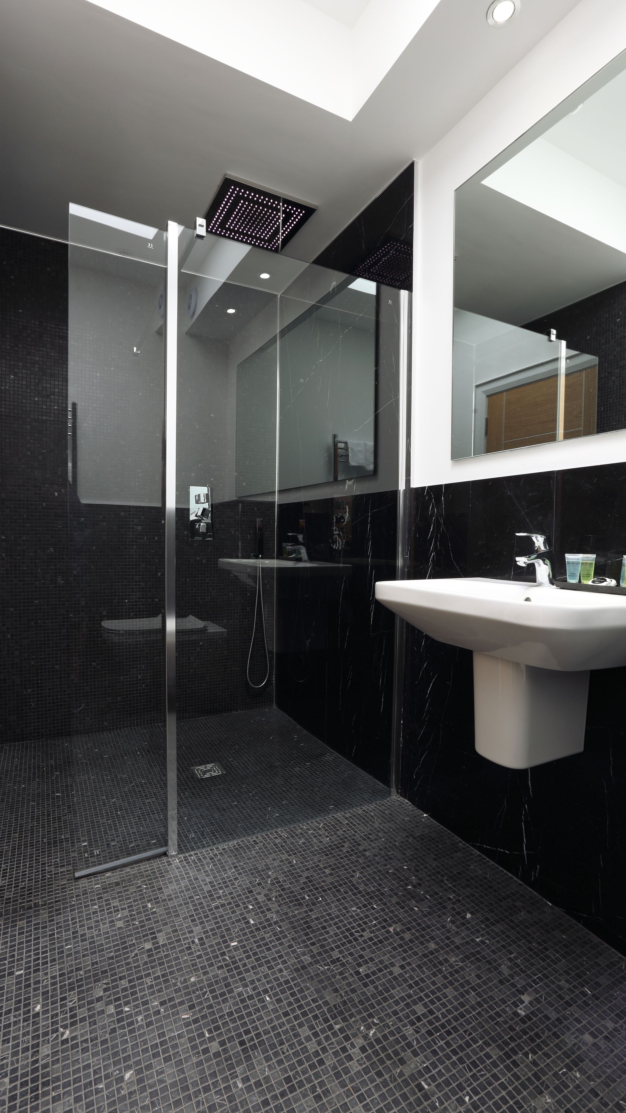 Un baño moderno con cabina de ducha de vidrio, un lavabo blanco y un espejo grande.