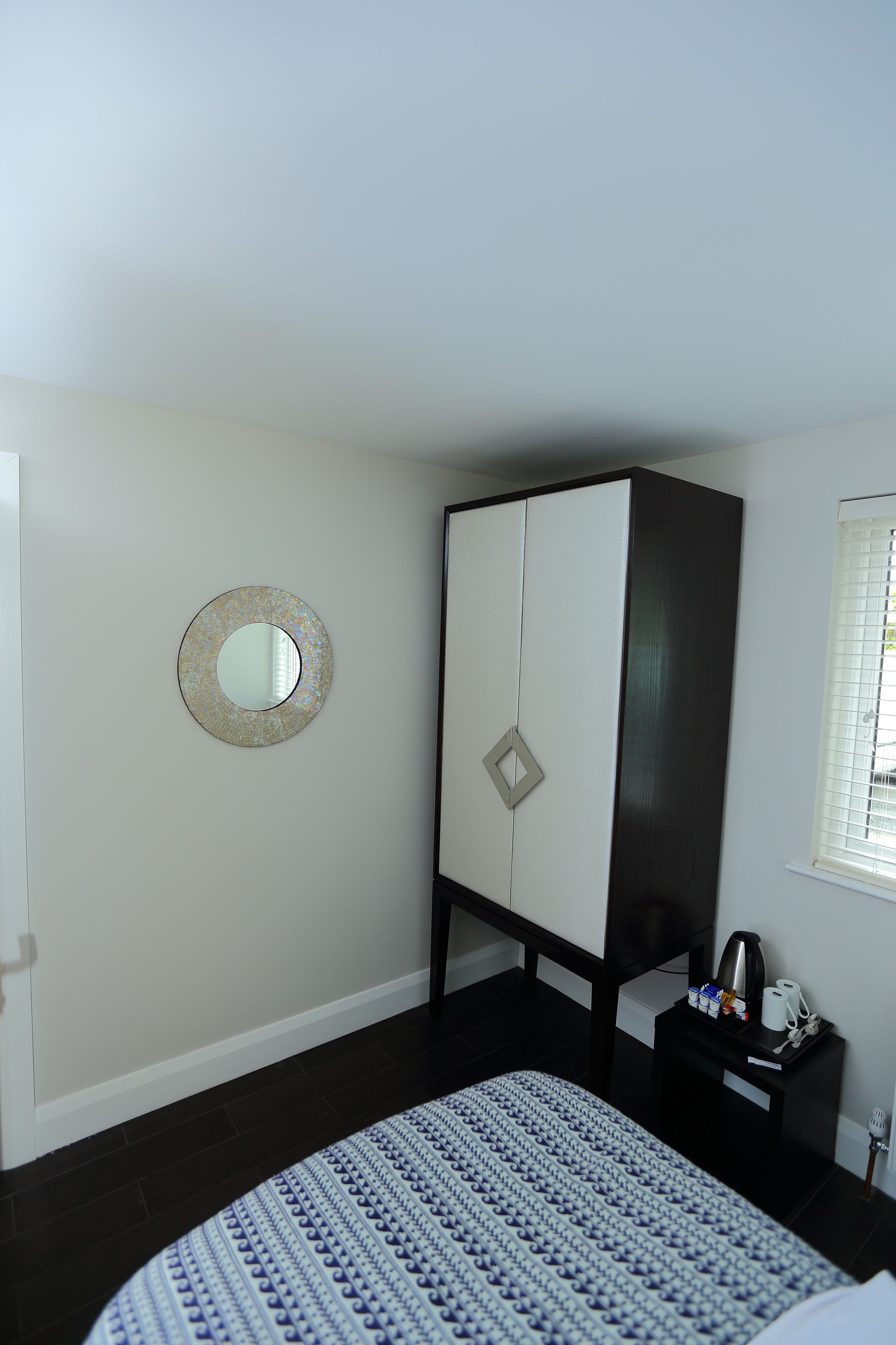 A bedroom with a bed, a wardrobe, a bedside table with a lamp, and a window with blinds.