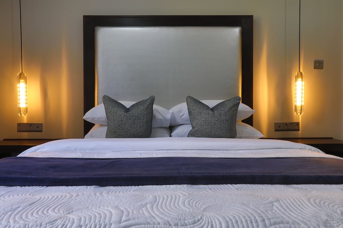 Una cama bien hecha con una colcha azul oscuro, dos almohadas y un cabecero.