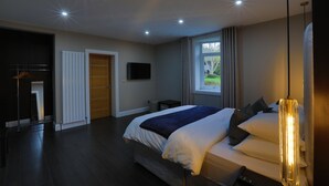 Ein modernes Hotelzimmer mit einem großen Bett, einem an der Wand befestigten Fernseher, einem Fenster mit Vorhängen und einer Decke mit Einbauleuchten.