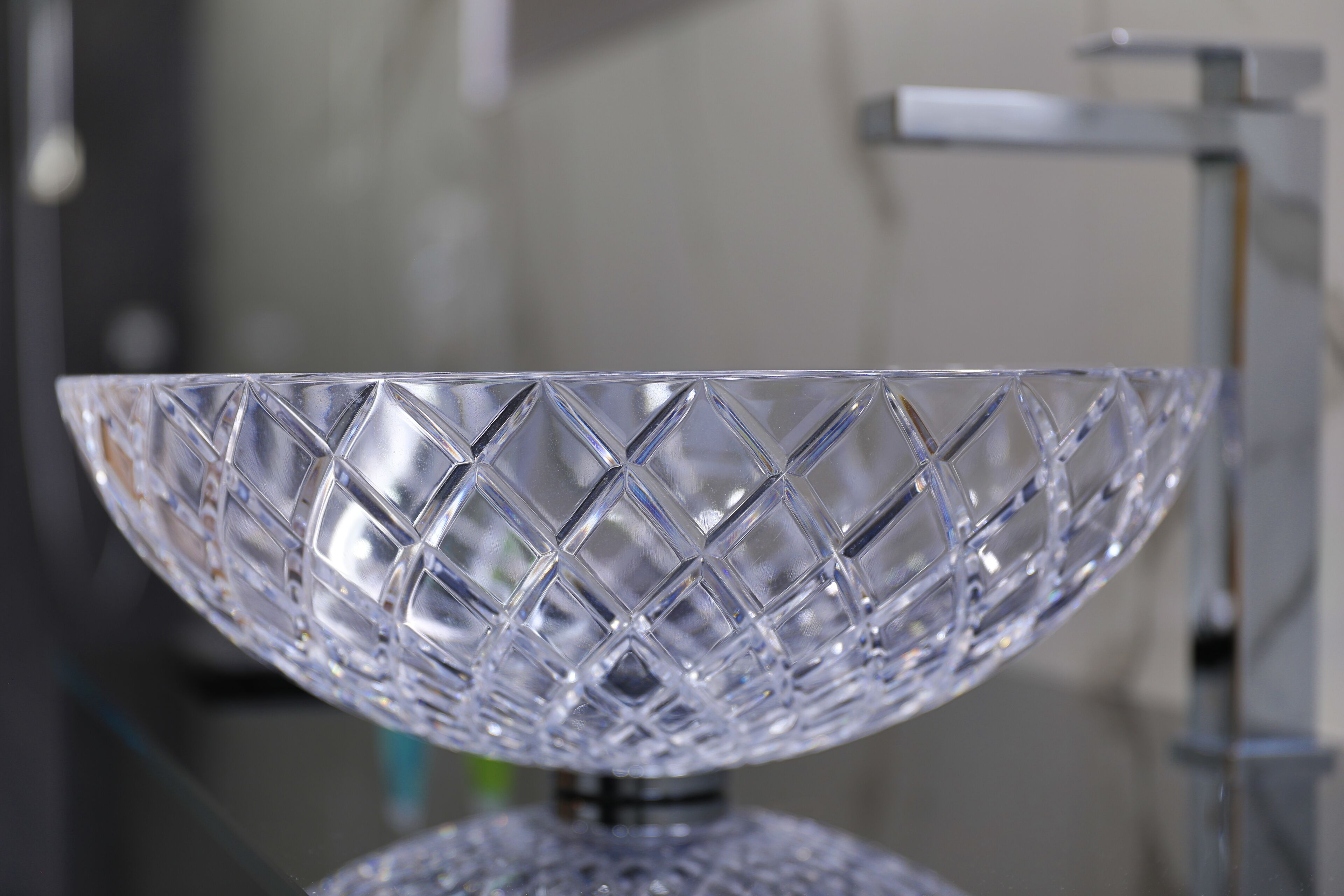 A clear glass bowl with a diamond pattern on a reflective surface.