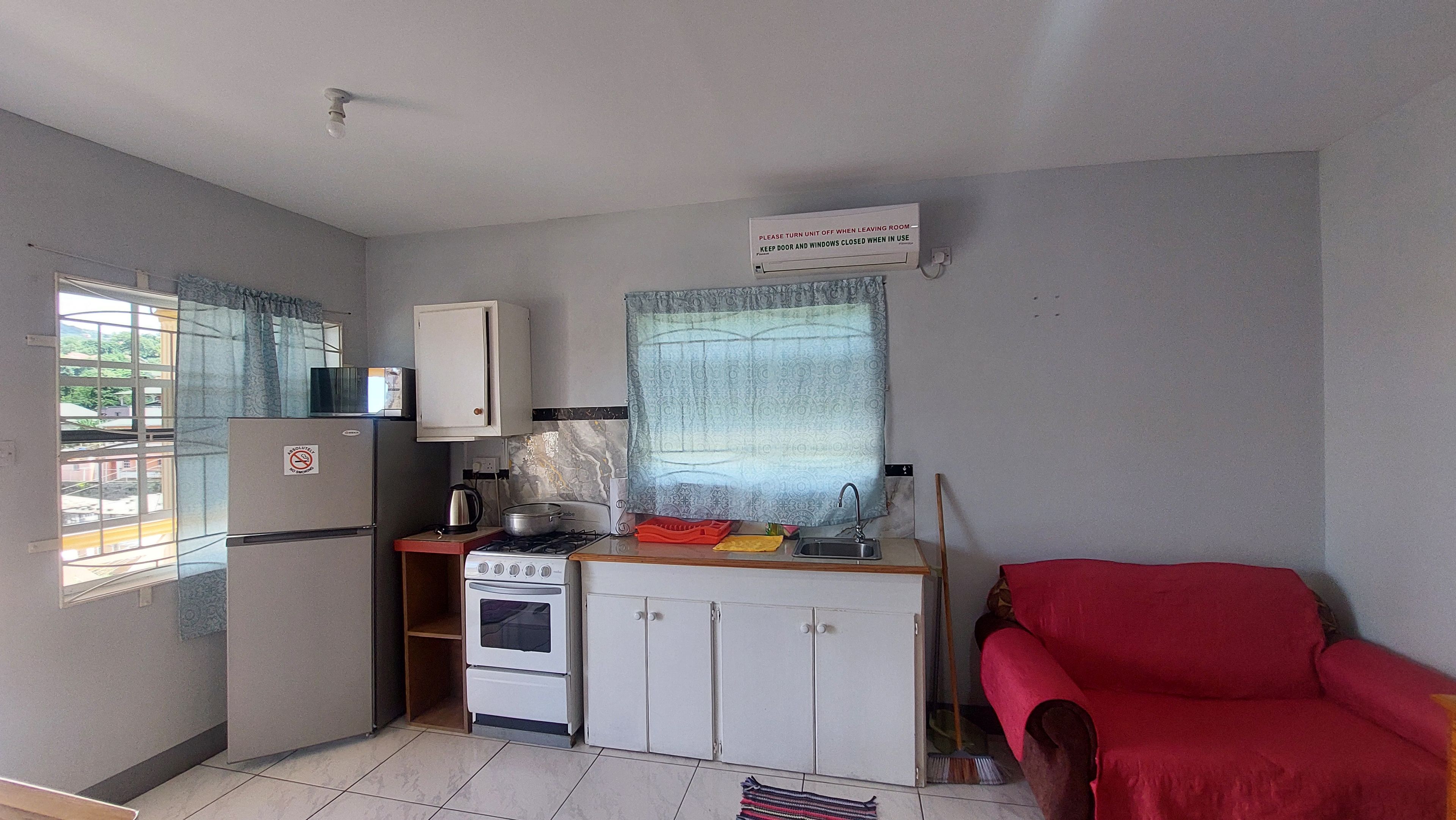 A compact kitchen with a refrigerator, stove, and microwave. There's a sign instructing to turn off the unit when leaving.