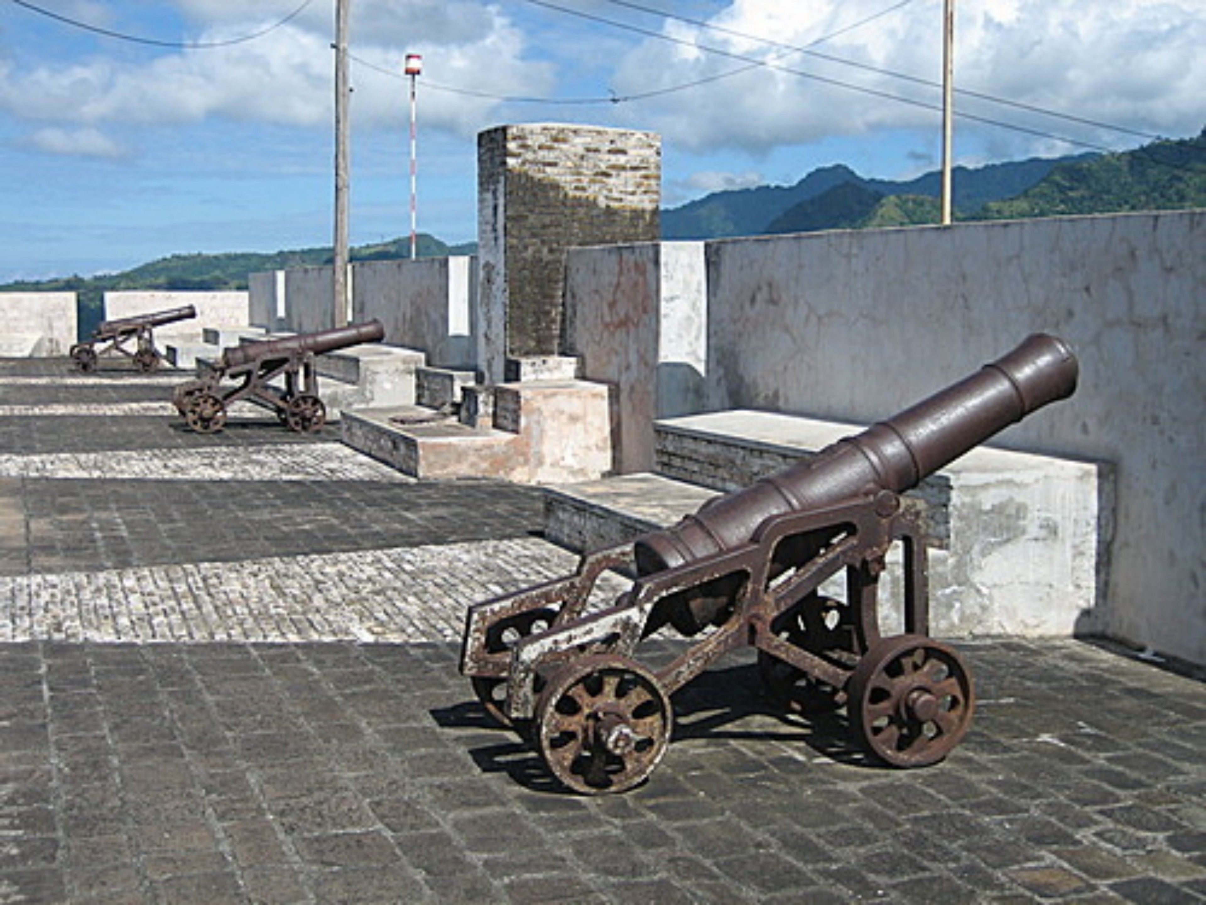 Un canon historique, placé sur un socle en pierre, avec une chaîne de montagnes en arrière-plan.