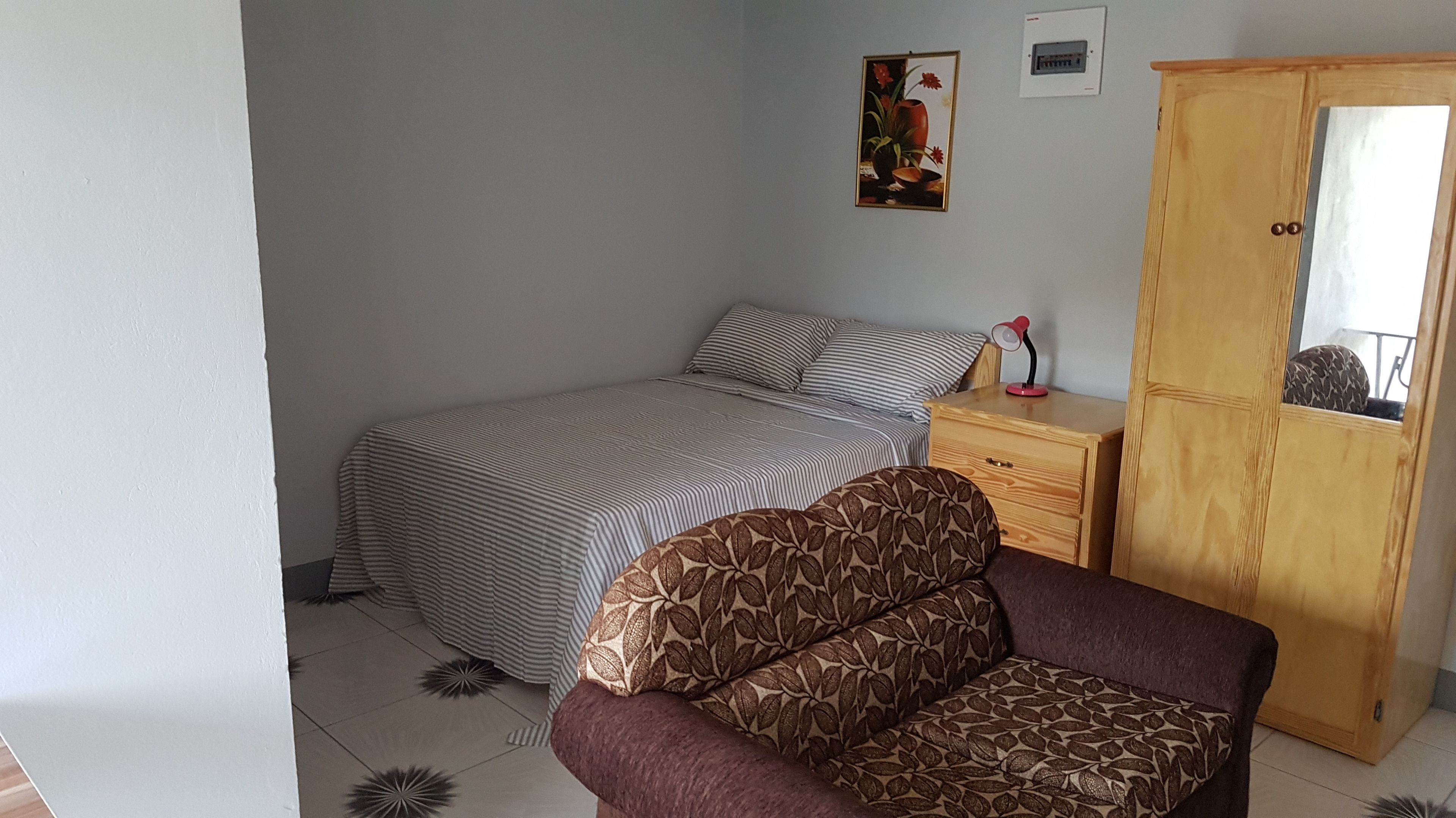 A bedroom with a bed, a wooden wardrobe, a nightstand, and a chair.
