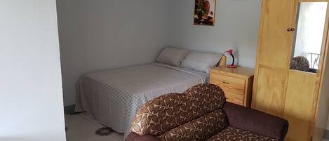 A bedroom with a bed, a wooden wardrobe, a nightstand, and a chair.