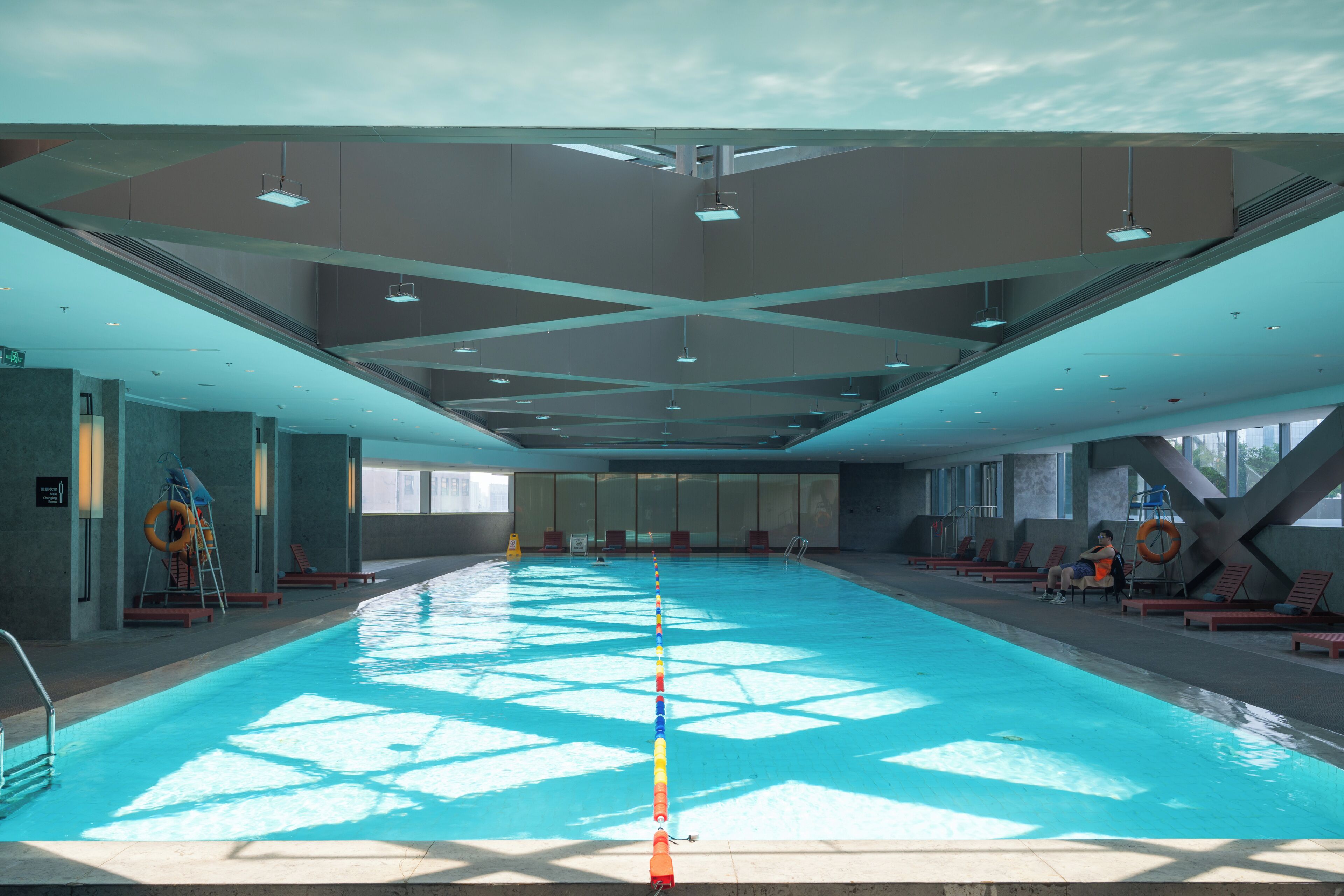 Uma piscina interior espaçosa com água azul cristalina, rodeada por espreguiçadeiras e cadeiras de banho.