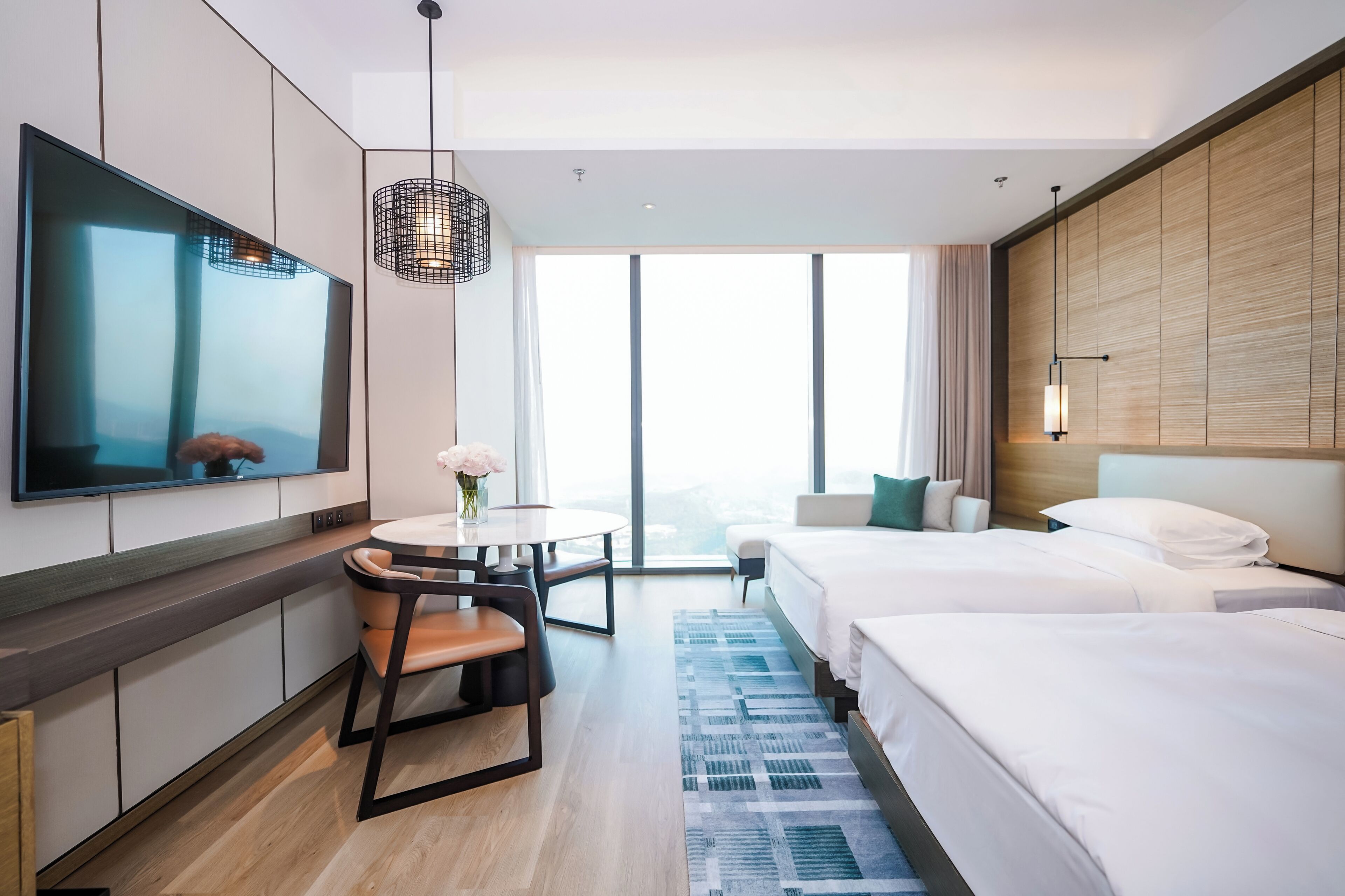 Ett modernt hotellrum med en platt-TV, en matplats med bord och stolar, en stor säng och utsikt över staden.