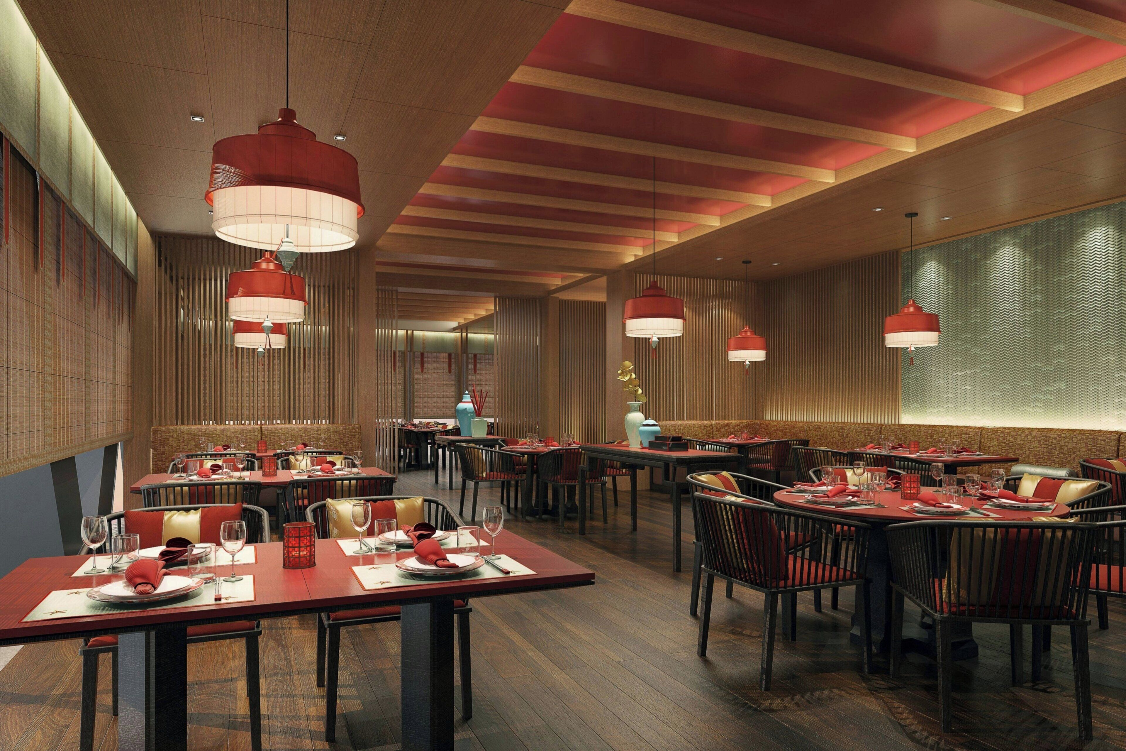 A modern restaurant interior with wooden floors, red and white pendant lighting, and neatly arranged tables and chairs.