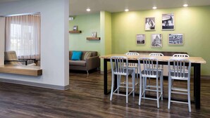 Un comedor moderno con una mesa de madera y sillas metálicas, un sofá con un cojín azul y una pared decorada con cuadros.