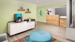 Una habitación de hotel moderna con kitchenette, un otomano azul y una alfombra colorida.