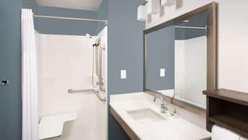 Un baño moderno con cabina de ducha, barras de apoyo, un espejo grande y un lavabo con toallero.