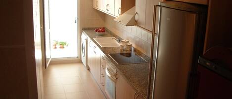 Una cocina con armarios de madera, un refrigerador de acero inoxidable, un fregadero y una lavadora.