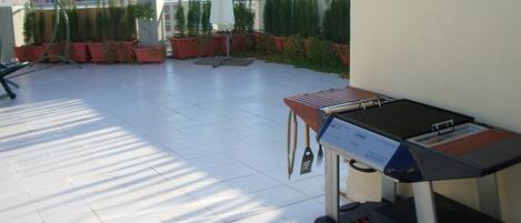 Terraza en la azotea con una parrilla, plantas en macetas y vistas de la ciudad.