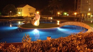 A swimming pool with a sculpture in the center, surrounded by a stone wall and a crowd of people. - Modern Penthouse Apartment on the Beach (Puig)