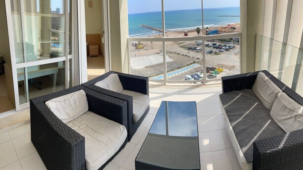 A balcony with wicker furniture, a glass table, and a view of the beach and parking lot. - Modern Penthouse Apartment on the Beach (Puig)