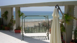 A balcony with a swing chair and an umbrella, overlooking a beach and ocean. - Modern Penthouse Apartment on the Beach (Puig)