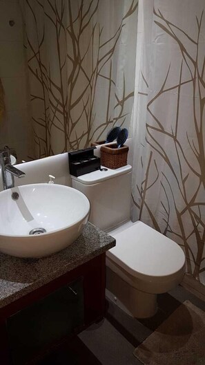A bathroom with a white sink, a toilet, and a shower curtain with a tree pattern.