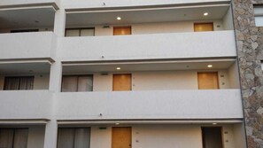 A multi-story hotel with balconies, each with a door and a small window.