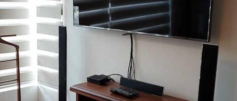 Una habitación con un televisor de pantalla plana grande montado en la pared, un mueble de madera debajo y una alfombra estampada en el suelo.