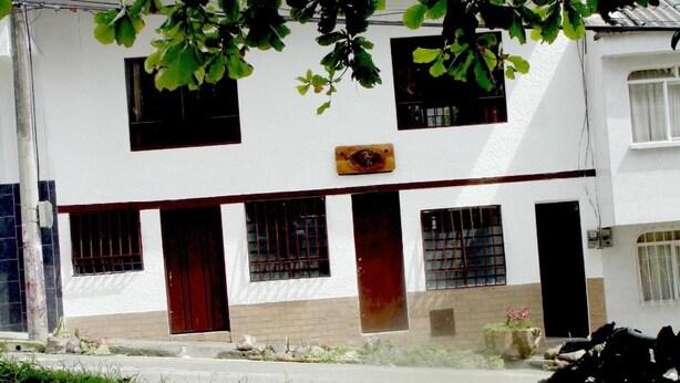 A two-story building with a white facade, multiple windows, and a red door. - Kfe L Hostel (Calarcá)