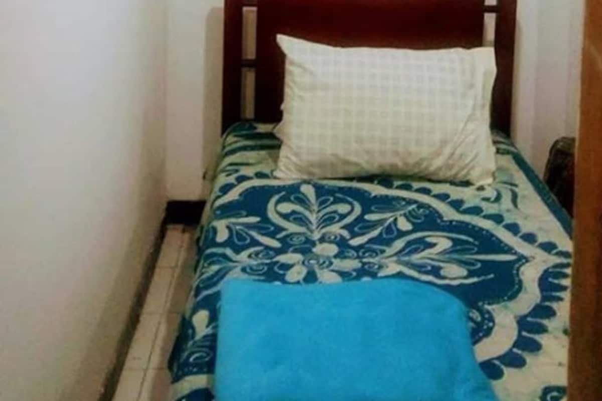 A small, narrow room with a single bed featuring a wooden headboard and a patterned bedspread.