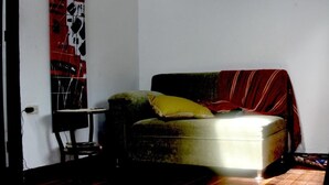 A small, dimly lit room with a single couch, a small table, and a large abstract painting on the wall. - Kfe L Hostel (Calarcá)