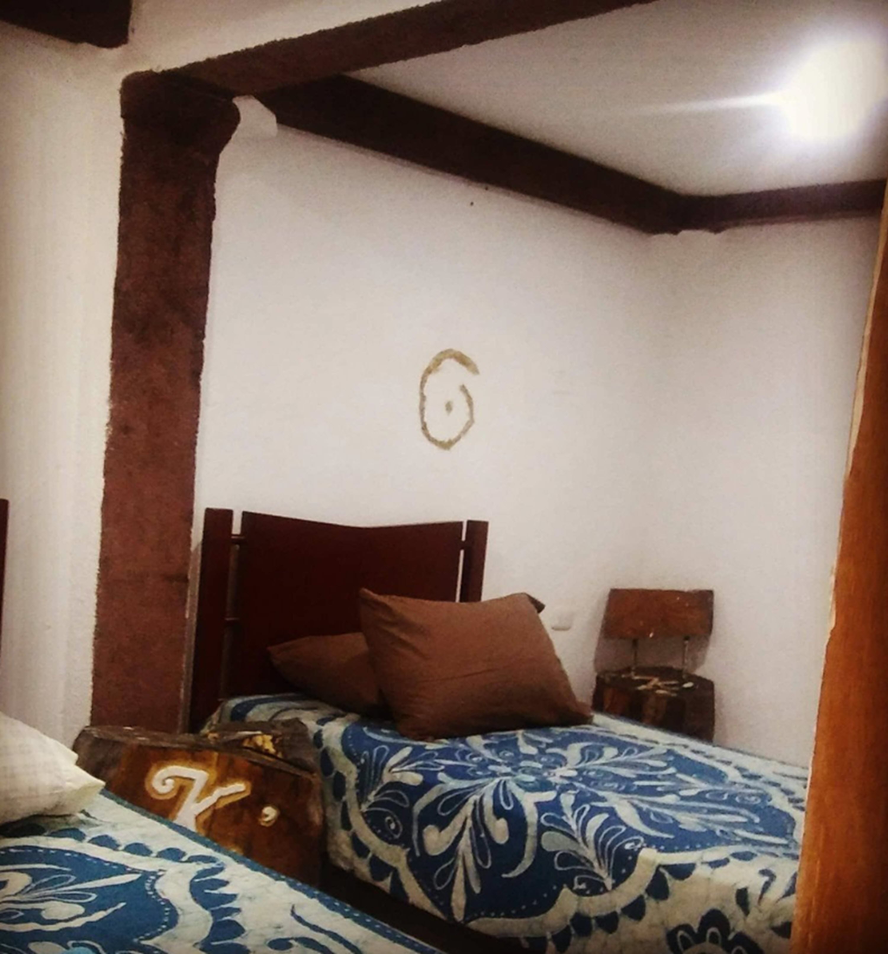 A bedroom with a wooden headboard, a patterned bedspread, a bedside table with a lamp, and a small decorative item on the nightstand.