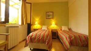 Una habitación con dos camas, una ventana con cortinas, un radiador y dos lámparas de noche.