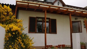 Una casa con porche de madera, fachada blanca y ventana con contraventanas.