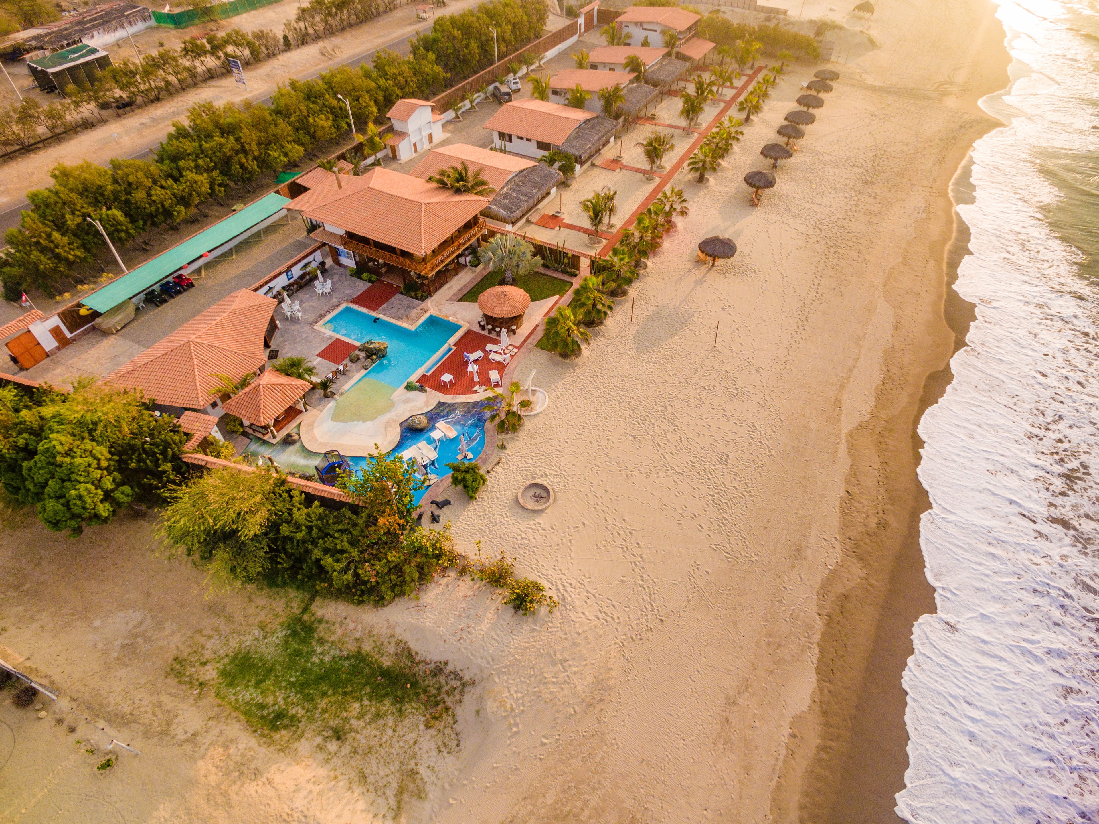 An aerial view of a resort with a swimming pool, beachside lounge, and beachfront villas.