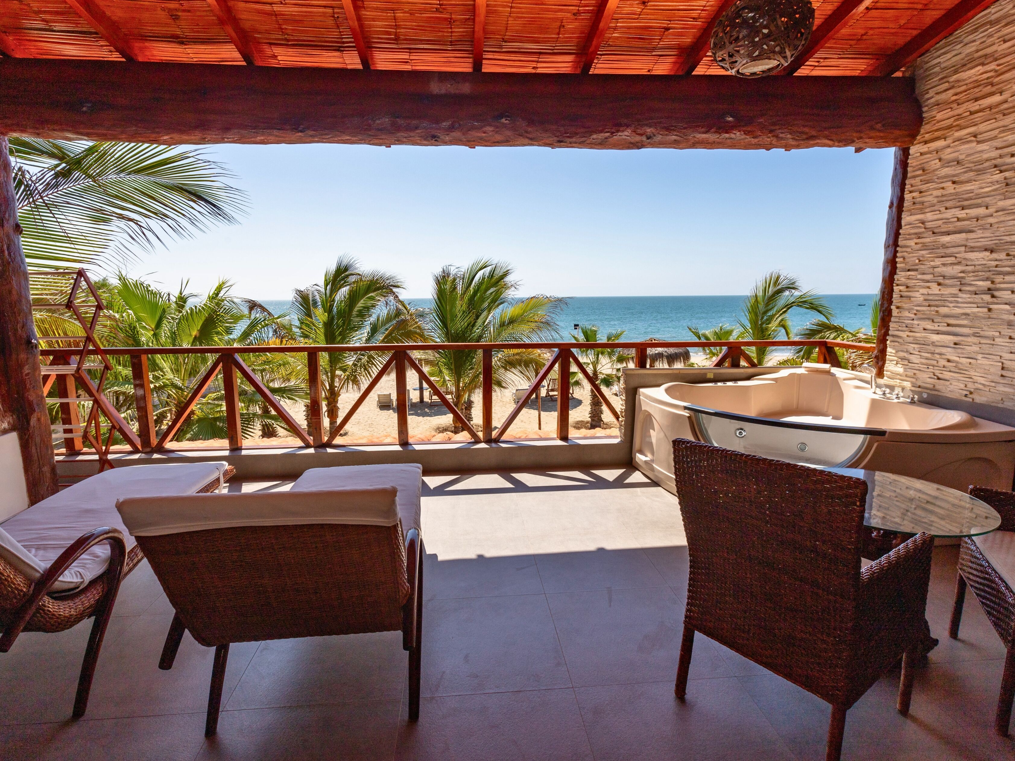 A balcony with wicker furniture, a hot tub, and a view of the beach and ocean.