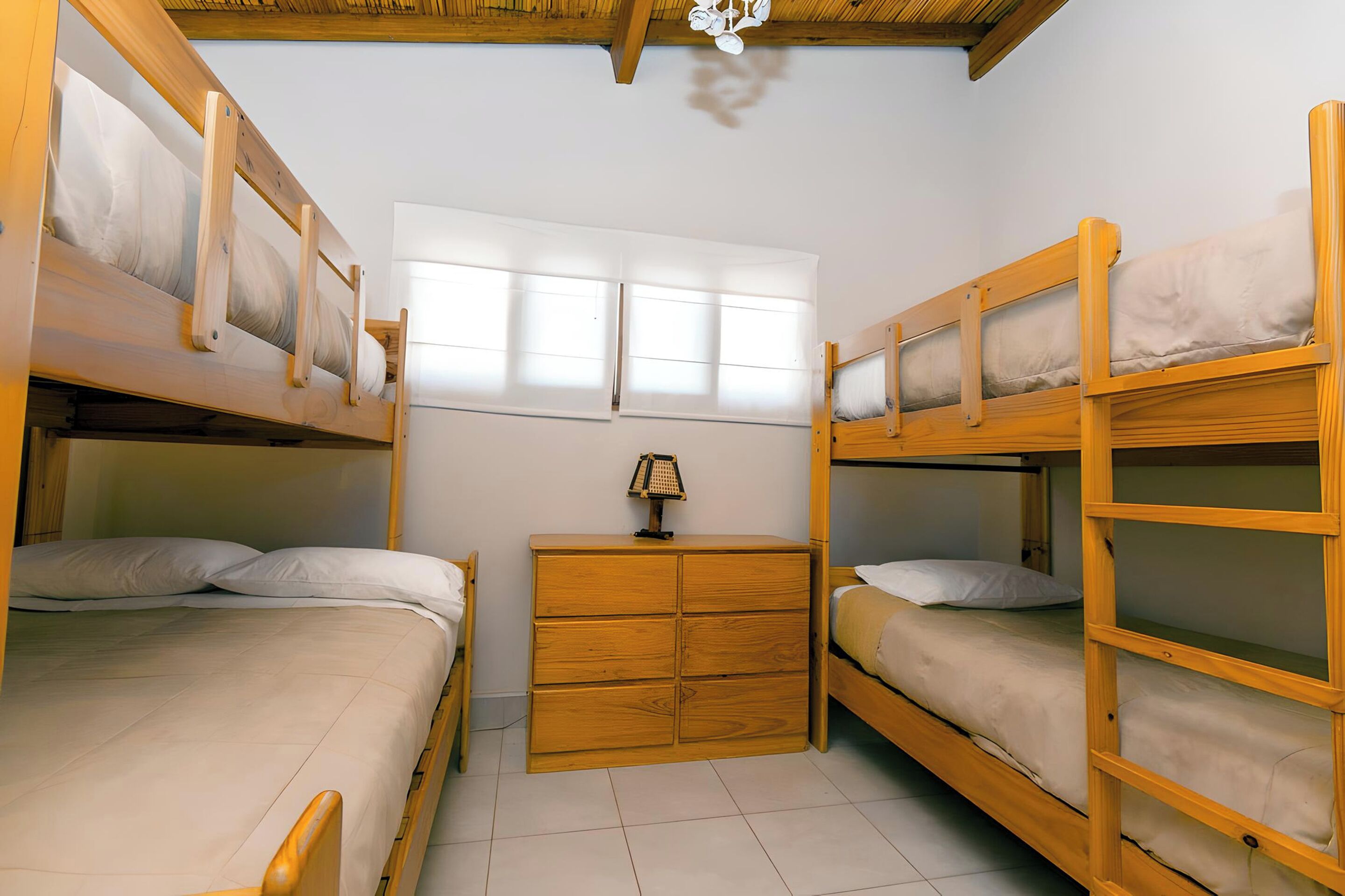 A room with bunk beds, a wooden dresser, and a window with blinds.