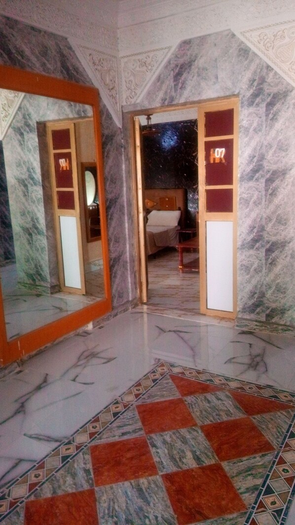 A room with a marble floor, a bed with a white headboard, and a large mirror on the left wall. - Hotel Raha (Nouakchott)