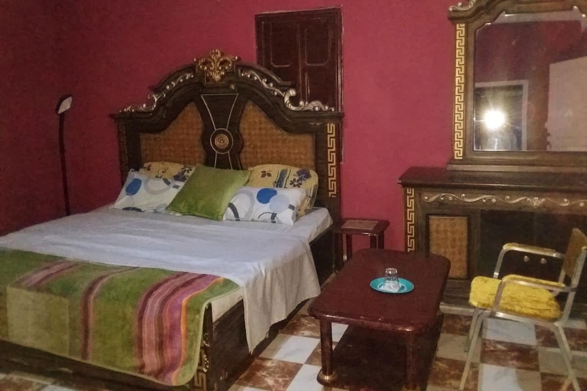 A bedroom with a bed, a nightstand, a chair, a table, a mirror, and a fireplace.