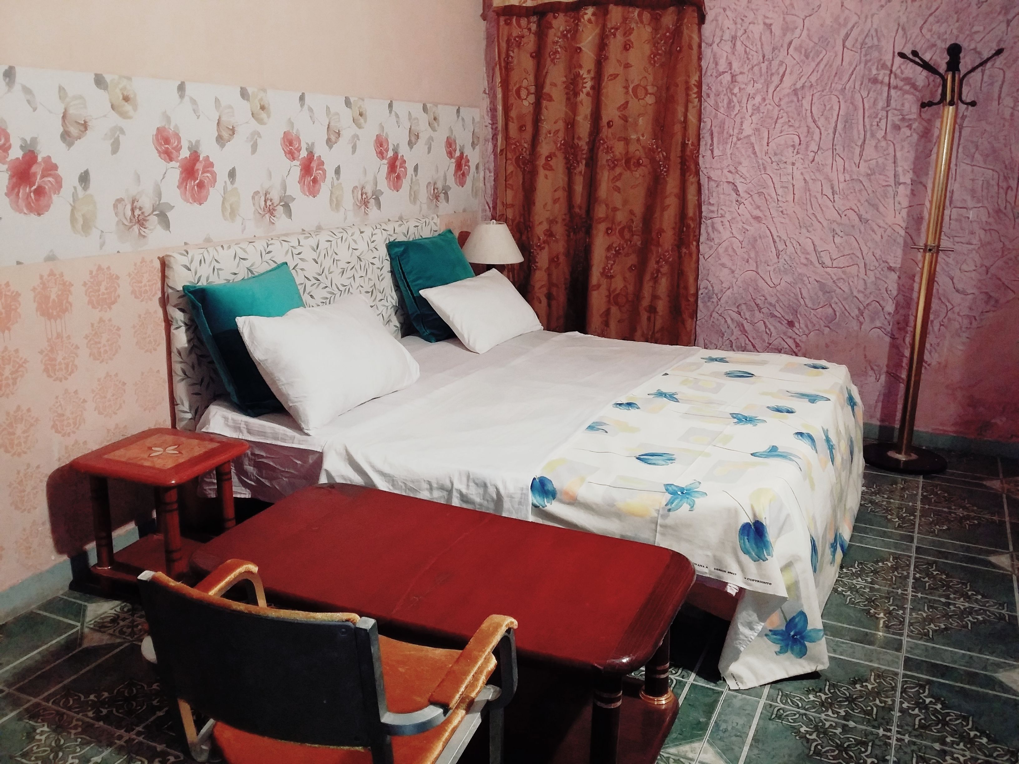 Un dormitorio con cama, almohadas, mesita de noche, silla y lámpara de pie.