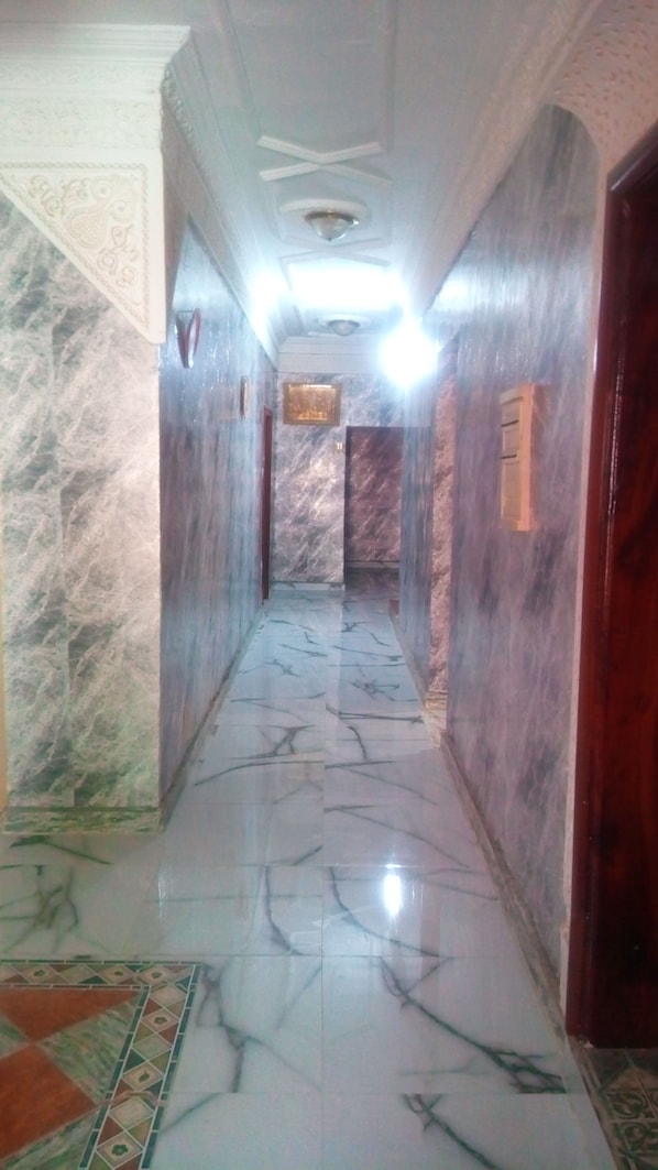 A marble-floored hallway with a ceiling light, marble walls, and a patterned carpet. - Hotel Raha (Nouakchott)