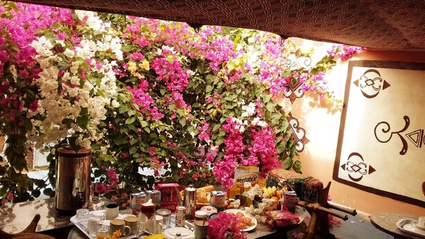 A table set with various items including a thermos, glasses, plates, and food containers, surrounded by a wall decorated with pink and white flowers. - Hotel Raha (Nouakchott)