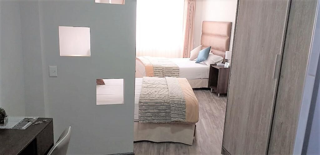 A hotel room with a bed, bedside table, lamp, and a wardrobe.