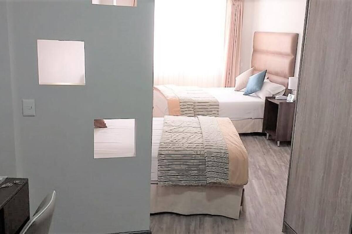 Una habitación de hotel con cama, mesita de noche, lámpara y armario.