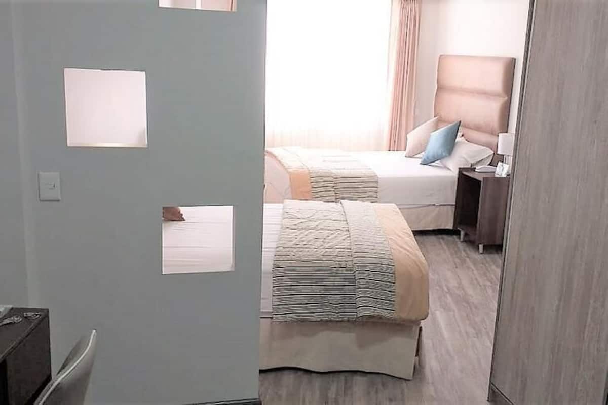 Una habitación de hotel con cama, mesita de noche, lámpara y armario.
