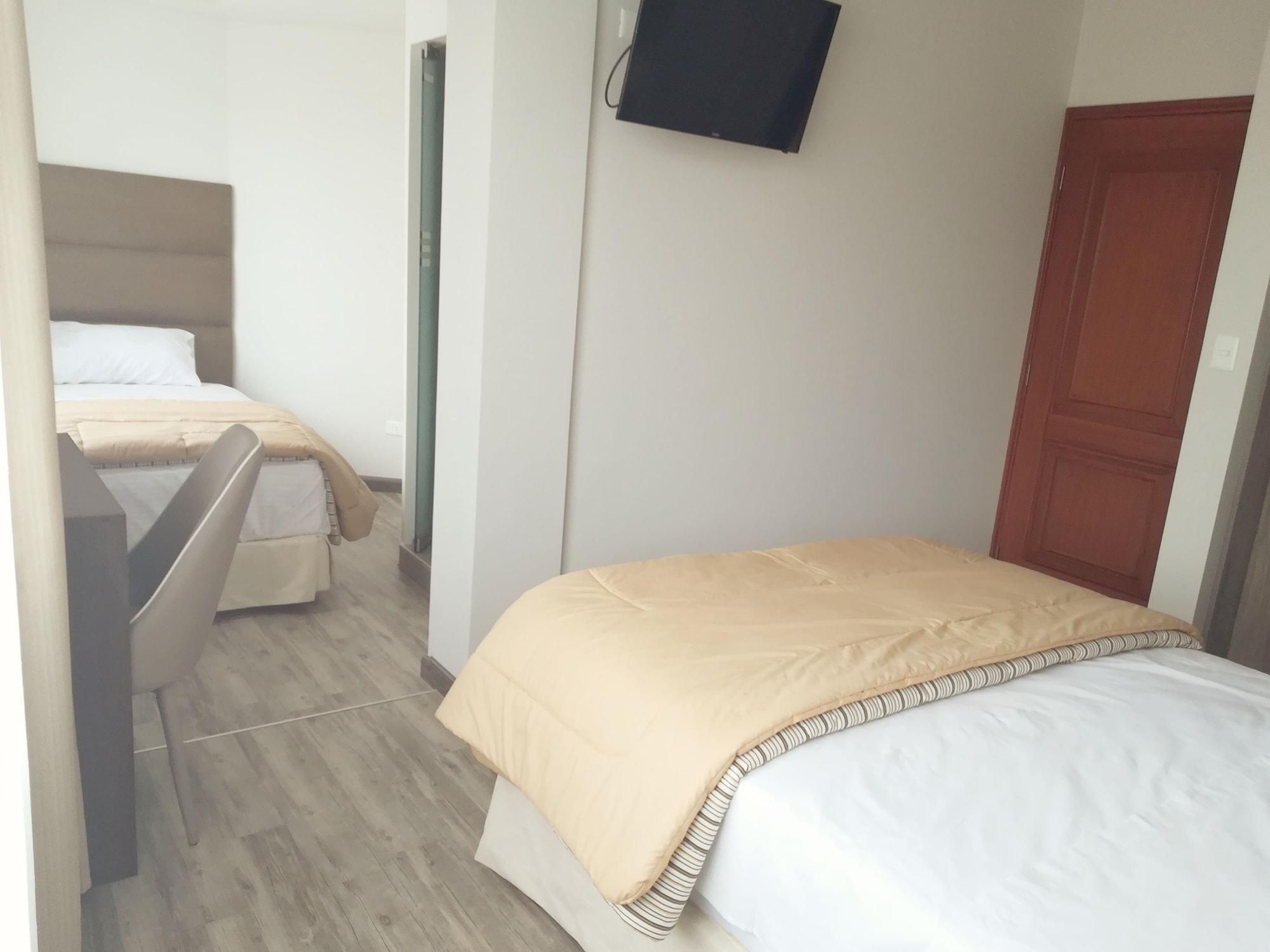 A hotel room with two beds, a television mounted on the wall, and a wooden door.