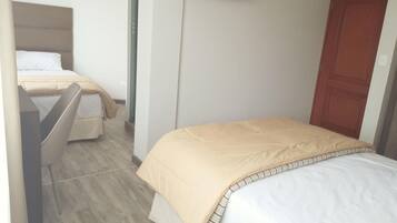 A hotel room with two beds, a television mounted on the wall, and a wooden door.
