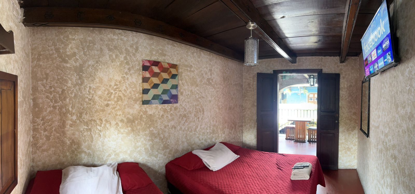 Une chambre avec deux lits, un luminaire suspendu, un téléviseur fixé au mur et une porte donnant sur l’extérieur.
