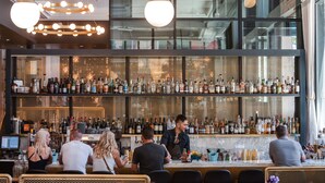 A bar with a high ceiling, modern pendant lighting, and a well-stocked liquor display. - The State Hotel (Seattle)